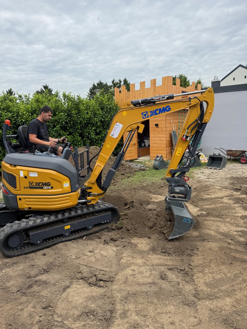 Minibagger bei Erdarbeiten vor einem hölzernen Gartenhaus